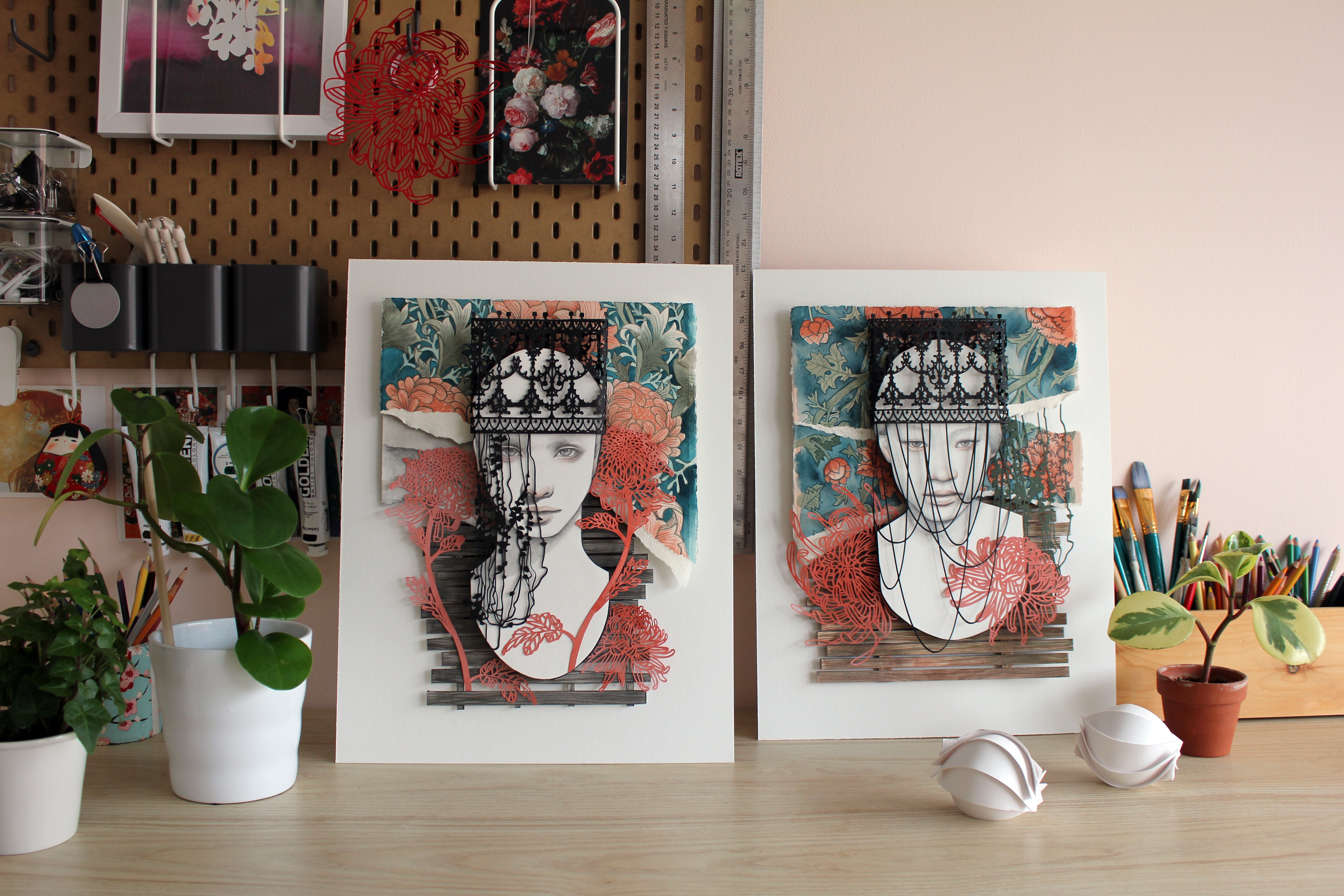 Stranger to Myself by Christine Kim – Two framed artworks on a desk with stationery items and plants.